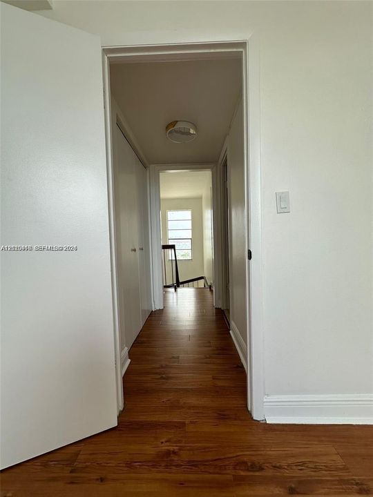 Hallway featuring wood-finish flooring, white doors, and a ceiling-mounted light fixture