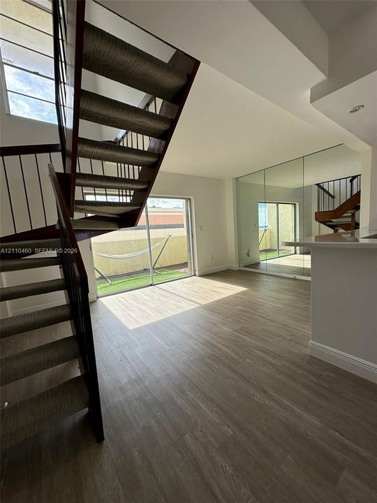 Open-concept interior featuring wood-finish flooring, a spiral staircase with metal railings, sliding glass doors, and floor-to-ceiling wall mirrors