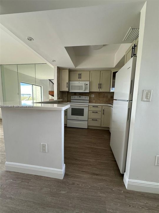 Kitchen featuring light-toned cabinetry, white appliance suite, neutral tile backsplash, solid-surface countertops, and wood-finish flooring