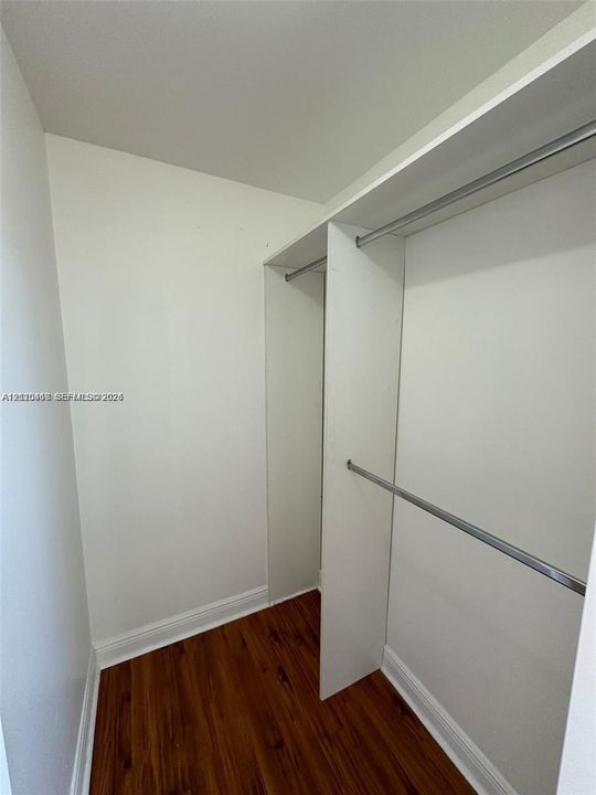 Walk-in closet featuring white built-in shelving, dual-tier metal hanging rods, and wood-finish flooring