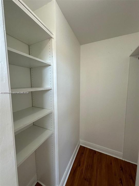 Storage area featuring floor-to-ceiling built-in shelving, white finish, and wood-finish flooring