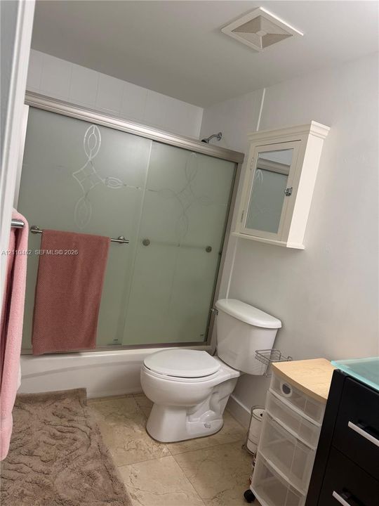 Bathtub with frosted glass sliding enclosure featuring decorative etching, wall-mounted medicine cabinet, and tile flooring