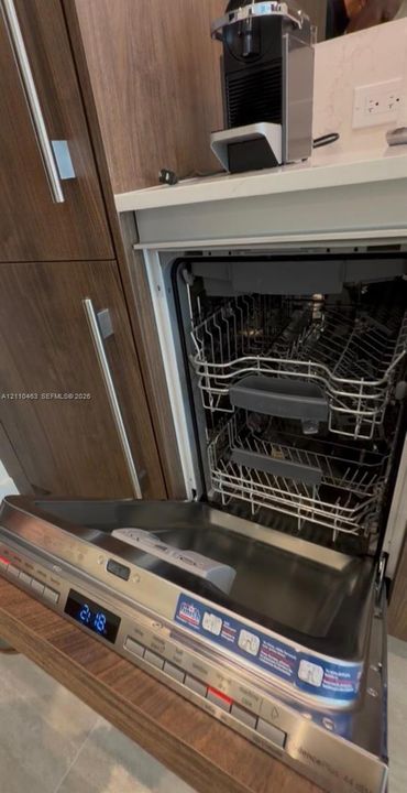 Built-in stainless steel dishwasher with integrated controls and stone-surface countertop featuring wood-finish cabinetry