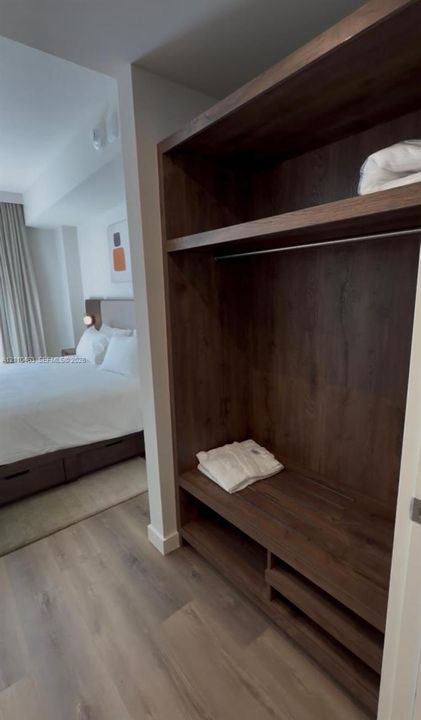 Built-in wardrobe featuring dark wood-finish cabinetry, integrated shelving, and a hanging rod, complemented by wood-finish flooring