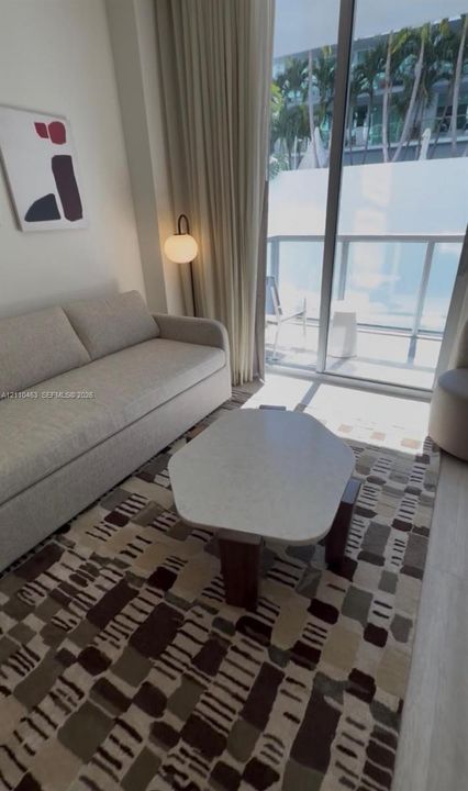 Floor-to-ceiling sliding glass door, private balcony with metal railing, and neutral wood-finish flooring