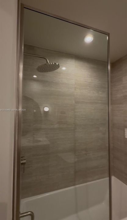 Shower featuring a stainless steel rainfall showerhead, glass enclosure with a metallic frame, and horizontal tile wall surfacing