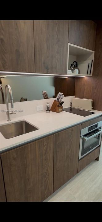 Wood-finish cabinetry, solid-surface countertops, undermount stainless steel sink, built-in cooktop, and integrated wall oven