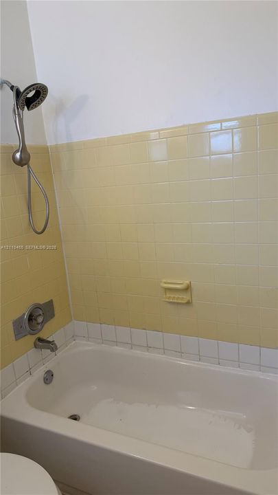 Bathtub with white porcelain finish, handheld showerhead, wall-mounted soap dish, and yellow ceramic tile surround