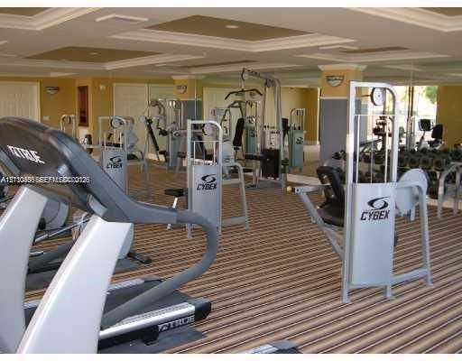 Fitness center featuring a recessed tray ceiling, mirrored walls, and striped carpet flooring