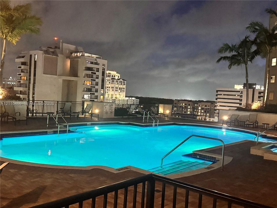 Swimming pool featuring a multi-level deck, integrated spa, perimeter metal fencing, and palm trees