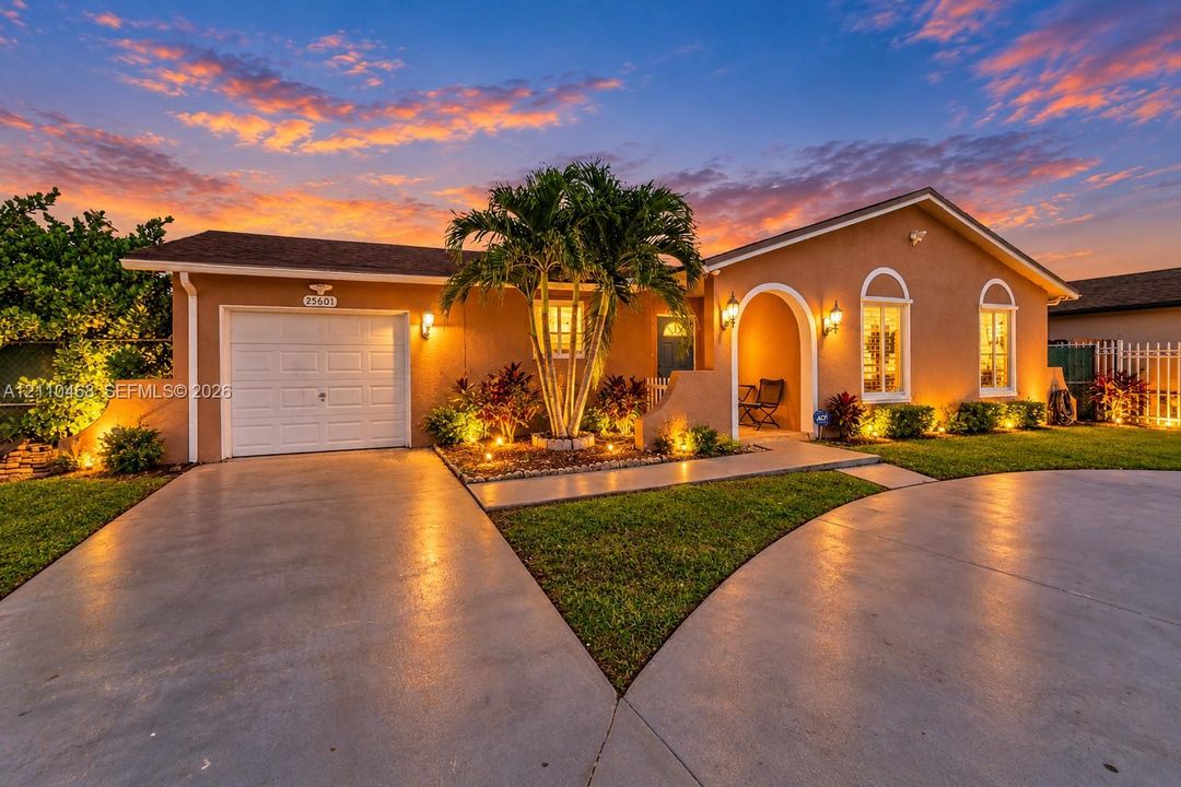 Single-story stucco exterior featuring an arched entryway, single-car garage, concrete driveway, and mature landscaping