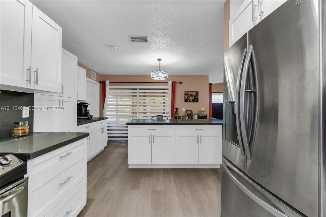 Kitchen featuring white shaker-style cabinetry, dark stone-finish countertops, stainless steel appliances, wood-finish flooring, and a central island