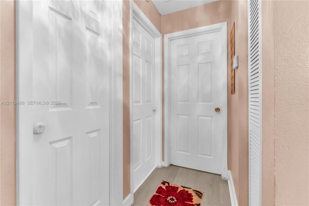 Interior hallway featuring wood-finish flooring, two six-panel doors with round hardware, and a louvered closet door