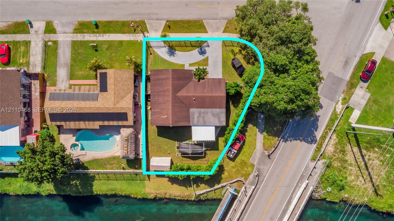 Corner lot property featuring water frontage, a concrete driveway, a covered patio, and established perimeter vegetation