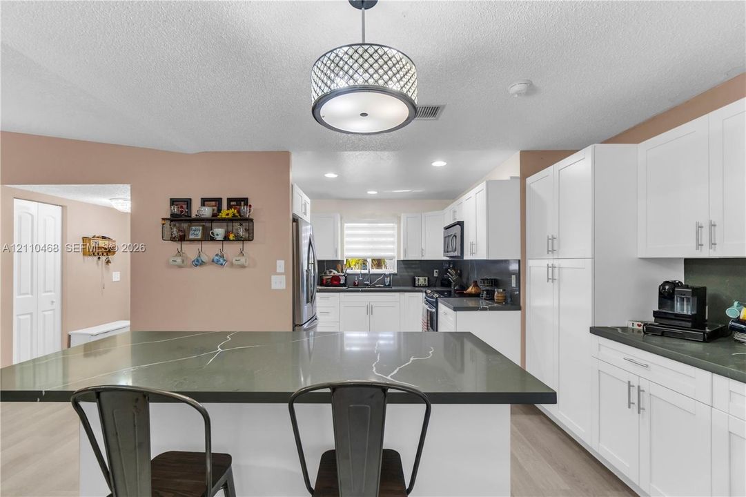 Kitchen featuring white shaker-style cabinetry, dark stone-finish countertops, a central island with a contrasting stone top, stainless steel appliances, and a geometric pendant light fixture