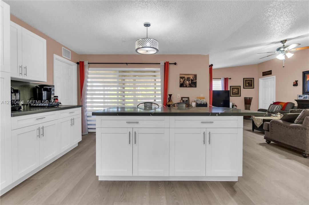 Kitchen featuring white shaker-style cabinetry, a central island with dark stone countertops, wood-finish flooring, and a contemporary drum pendant light fixture