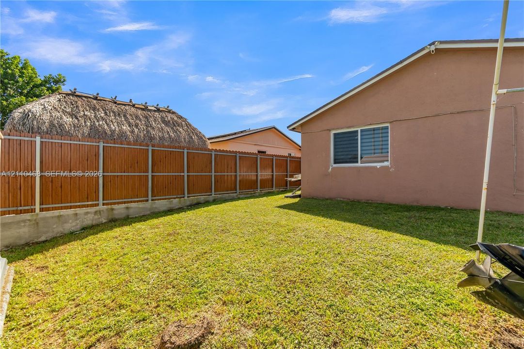 Rear yard featuring a manicured lawn, concrete retaining wall, and horizontal wood-panel fencing
