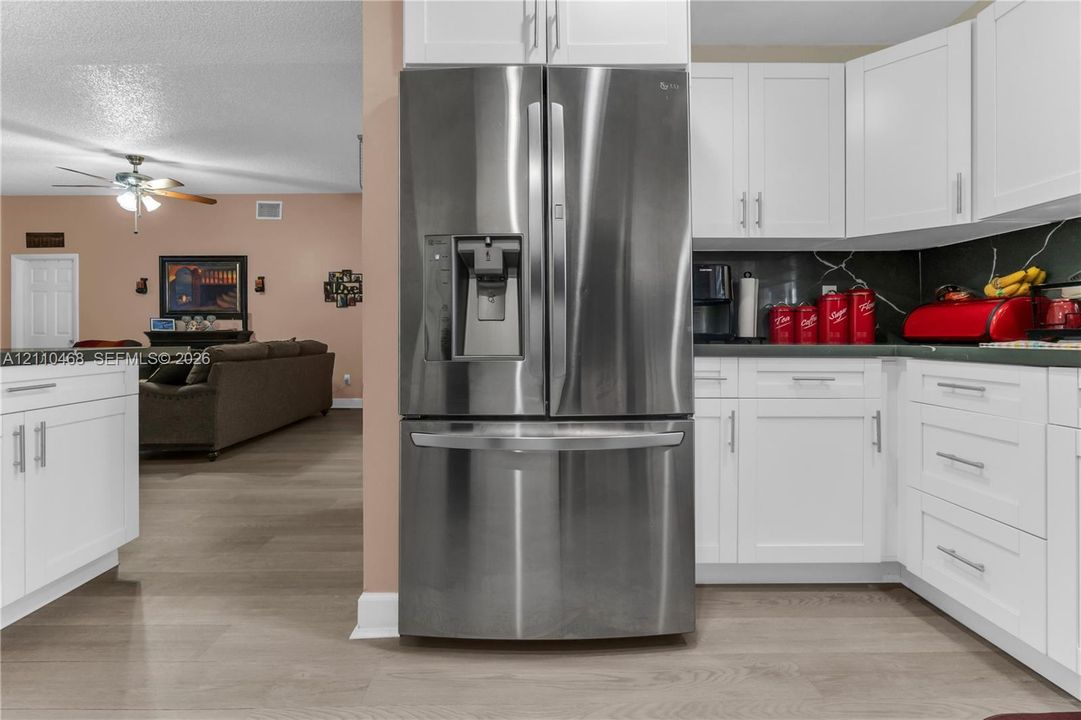 Kitchen featuring white shaker-style cabinetry, stainless steel French-door refrigerator, and wood-finish flooring
