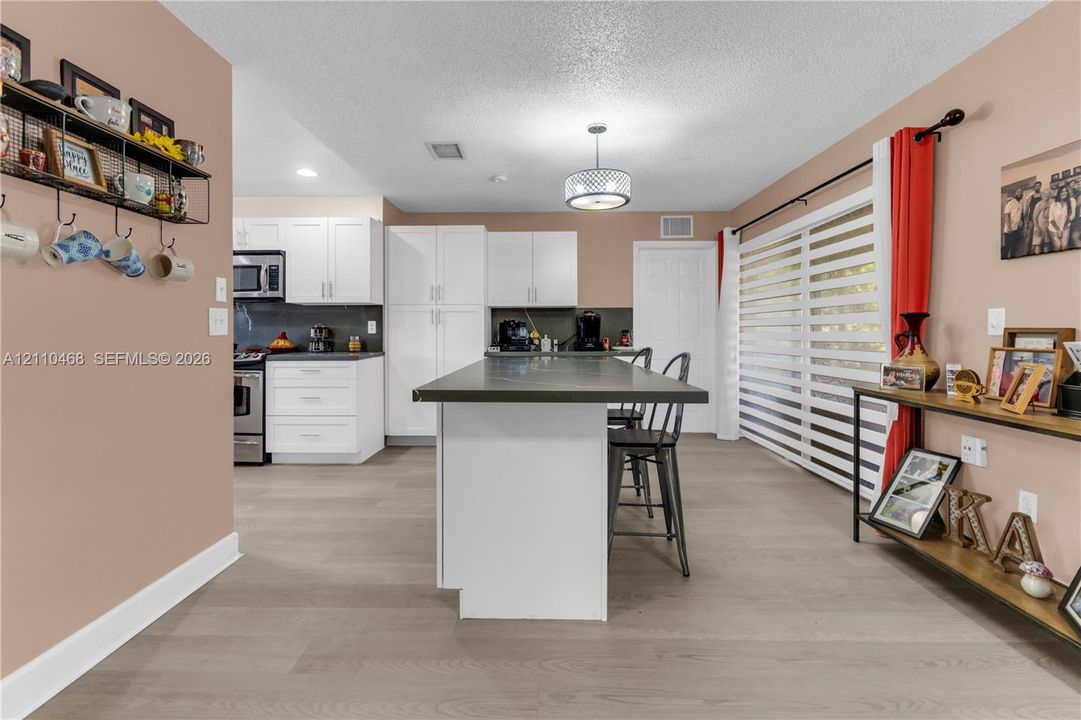 Kitchen featuring white cabinetry, an island with a solid surface countertop, wood-finish flooring, and horizontal blind window coverings