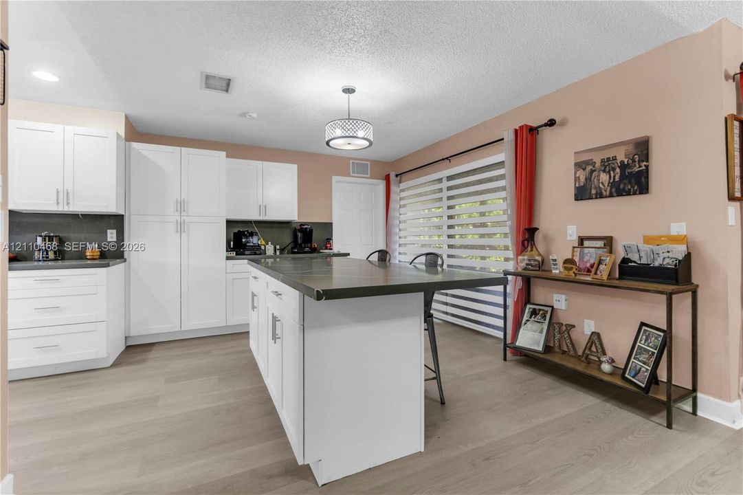 Kitchen featuring white cabinetry, a center island with an integrated countertop, wood-finish flooring, and a drum-style pendant light