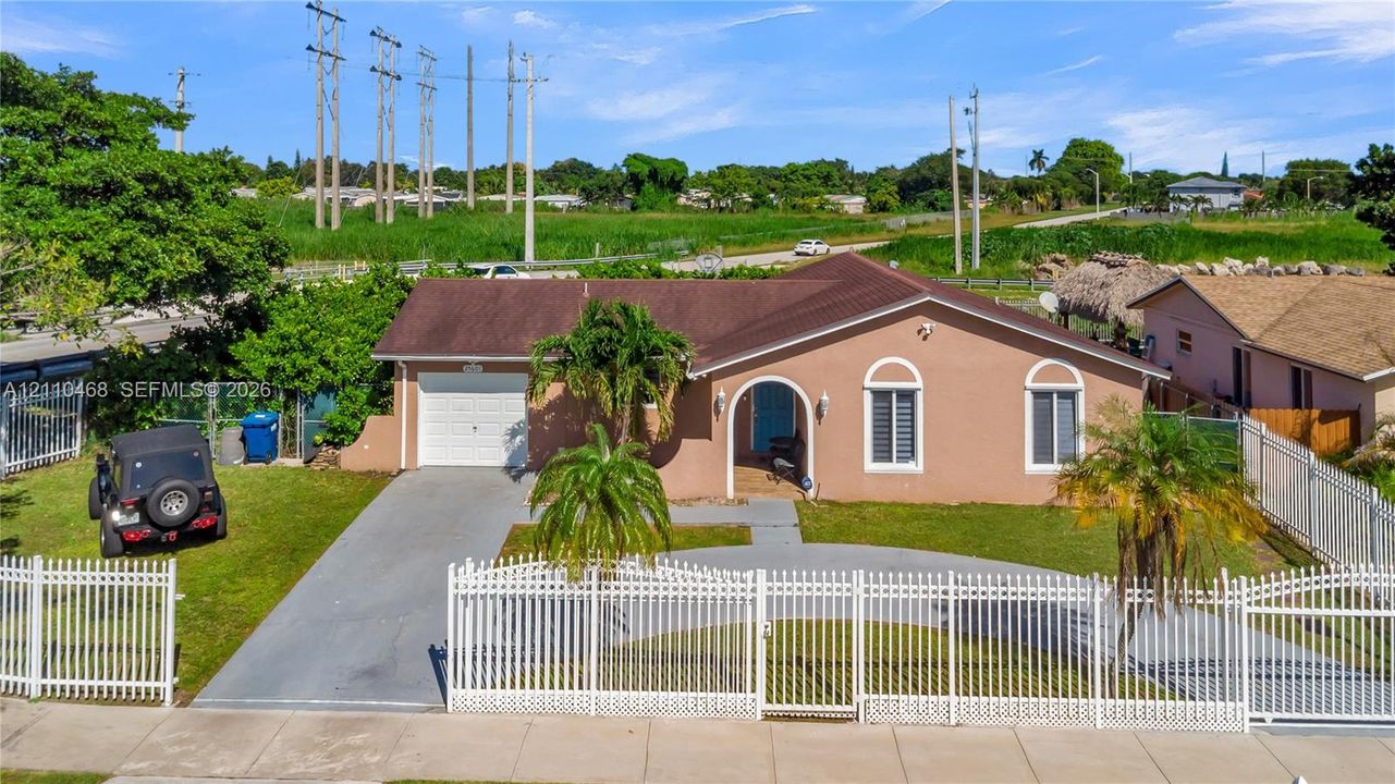 Single-story residence featuring a stucco exterior, arched window detailing, an attached garage, and full-property white picket-style perimeter fencing
