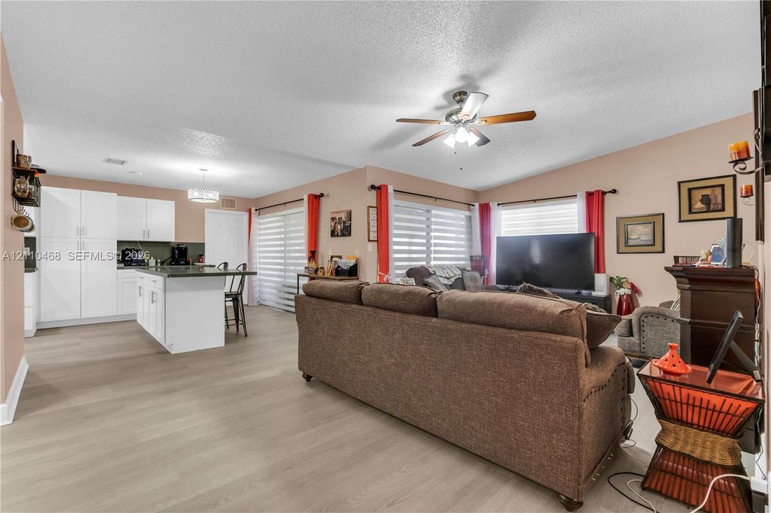 Open-concept interior featuring wood-finish flooring, a kitchen island, white cabinetry, and a ceiling fan with integrated lighting