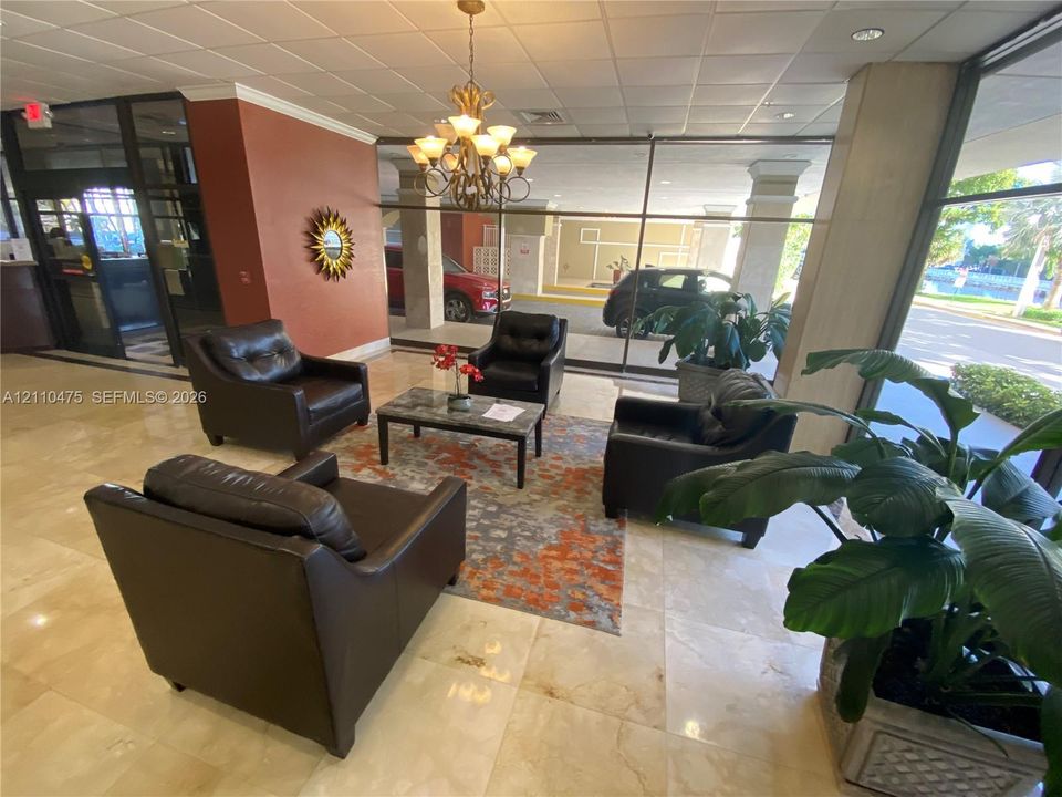 Lobby area featuring polished stone flooring, a multi-light chandelier, floor-to-ceiling glass paneling, and structural columns
