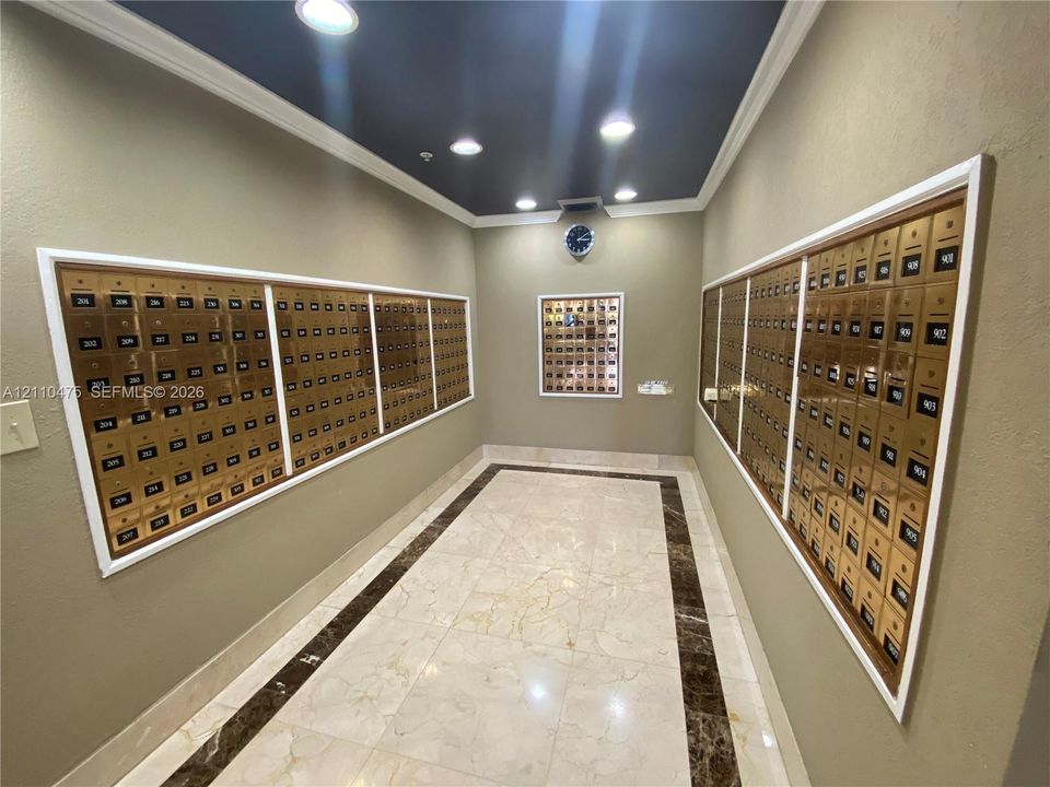 Mail center featuring recessed metal mailboxes, polished tile flooring with contrasting stone-finish border inlay, crown molding, and recessed lighting