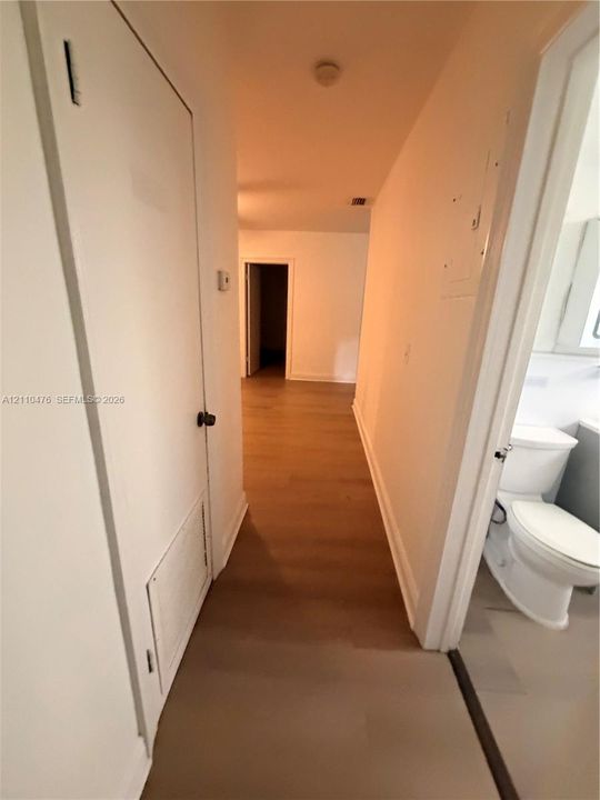 Hallway featuring wood-finish flooring, solid-core doors, and neutral paint finishes, with access to a bathroom containing a porcelain toilet