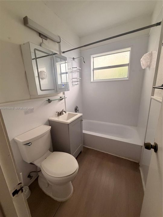 Bathroom featuring wood-finish flooring, a grey vanity with a square sink, a mirrored medicine cabinet, and a bathtub with a shower surround