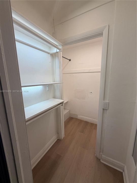 Storage closet featuring white built-in shelving, a garment rod, and wood-finish flooring