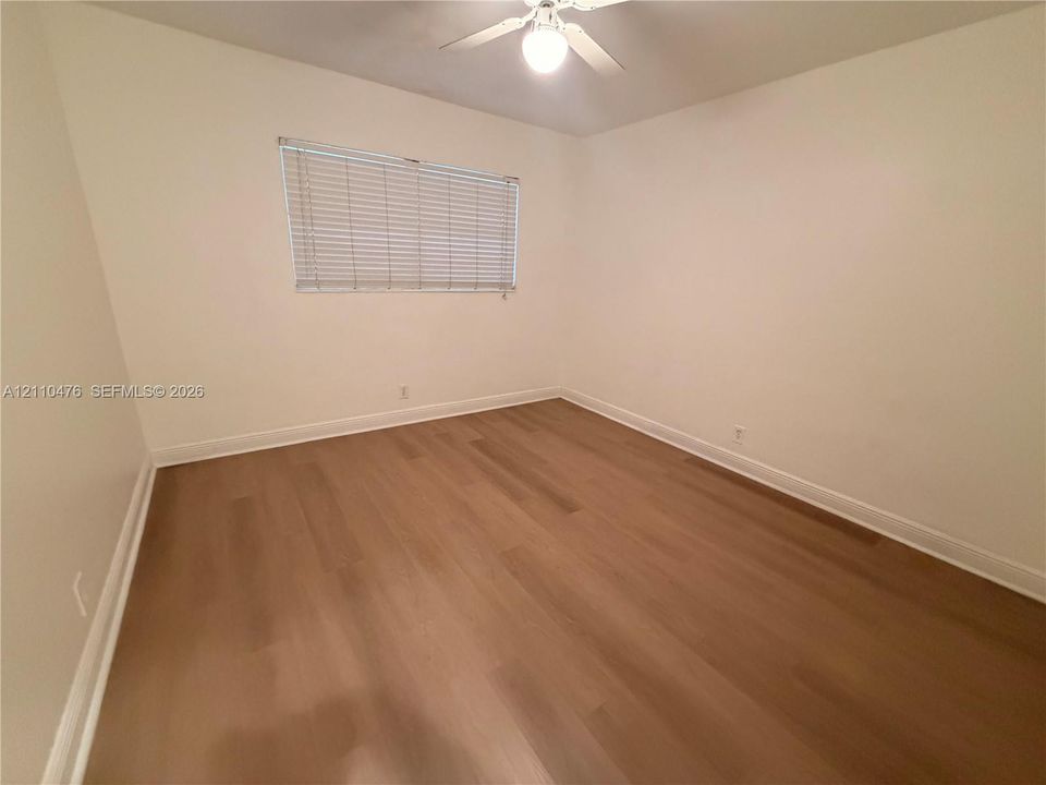 Neutral interior room featuring wood-finish flooring, white walls, and a ceiling fan with integrated lighting