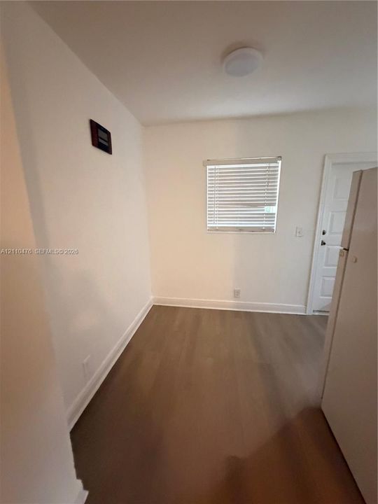 Neutral-toned walls, wood-finish flooring, a single-hung window with blinds, and a flush-mount ceiling light fixture
