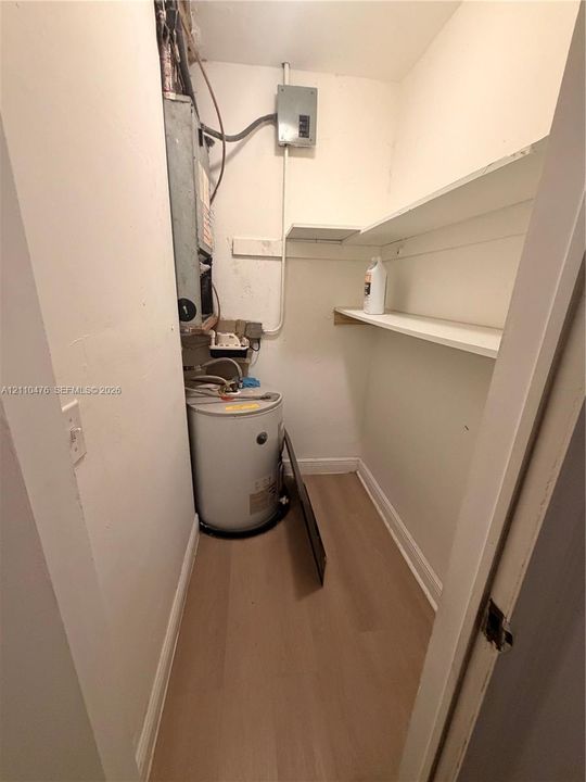 Utility closet featuring wood-finish flooring, two fixed wall-mounted storage shelves, and an electric water heater