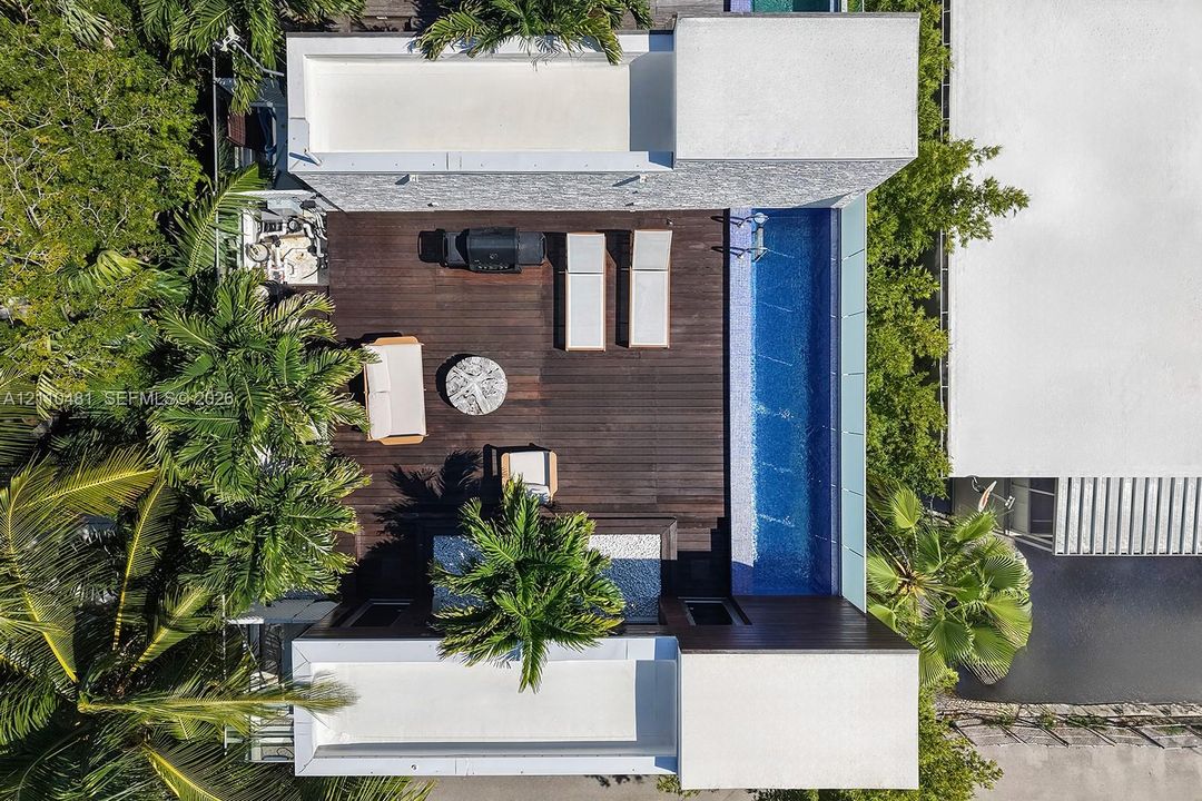 Expansive wood-finish decking featuring a built-in swimming pool, integrated hardscaping, and surrounding mature tropical vegetation