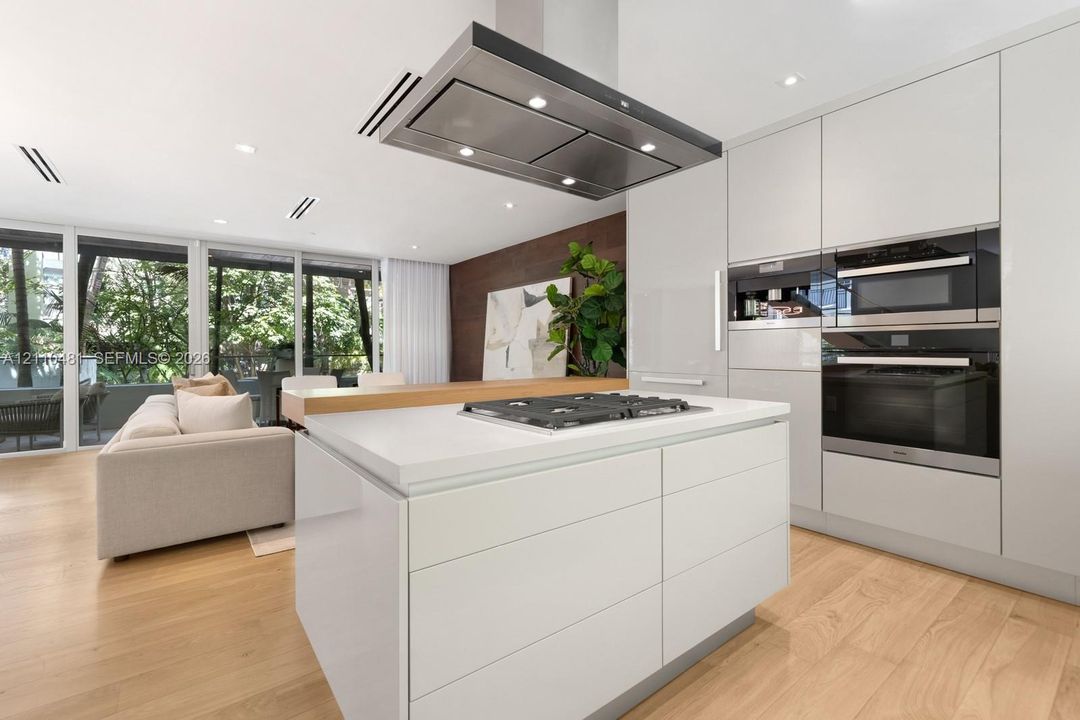 Kitchen featuring flat-panel cabinetry, center island with a gas cooktop, built-in wall ovens, stainless steel ceiling-mounted vent hood, and wood-finish flooring
