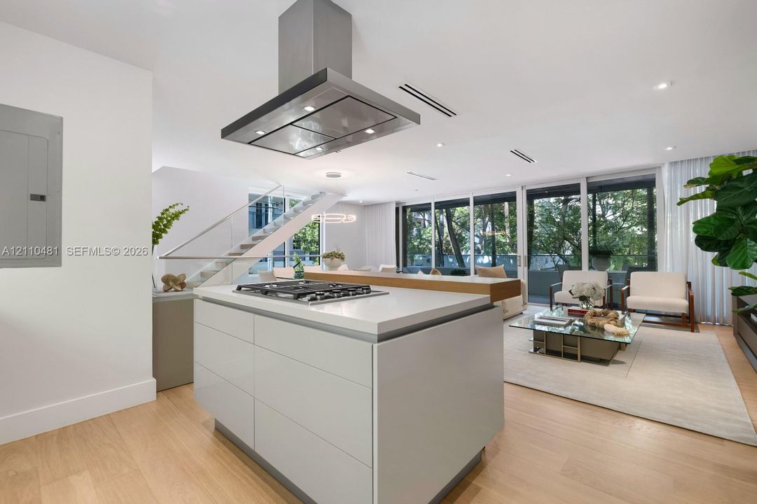 Kitchen island featuring a stone countertop, inset gas cooktop, and stainless steel hood range, complemented by wood-finish flooring and floor-to-ceiling windows