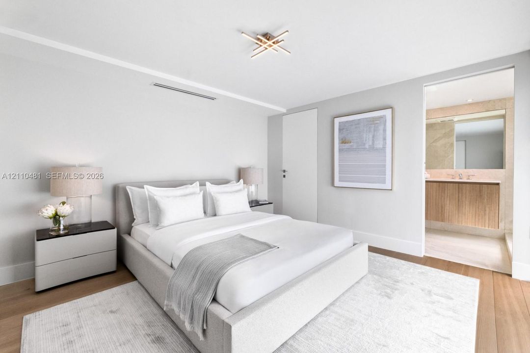Modern bedroom featuring wide-plank wood-finish flooring, a linear ceiling light fixture, and an ensuite bathroom with a floating vanity and natural stone wall accents