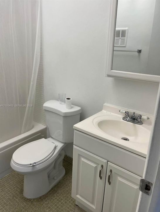 Bathroom featuring a white vanity cabinet with a integrated sink, dual-handle faucet, white medicine cabinet, and a shower-tub combination with a tiled surround