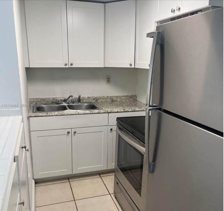 Kitchen featuring white shaker-style cabinetry, speckled stone-patterned countertops, a double-basin stainless steel sink, tile flooring, and stainless steel appliances