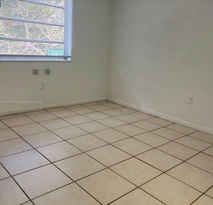 Neutral interior space featuring ceramic tile flooring, solid wall construction, and horizontal window blinds