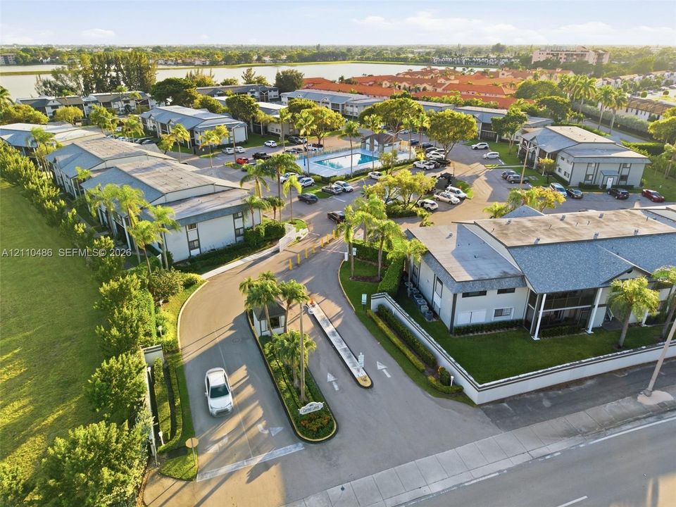 Gated residential community featuring paved access roads, a centralized swimming pool, multi-unit buildings with shingle roofing, and mature landscaping