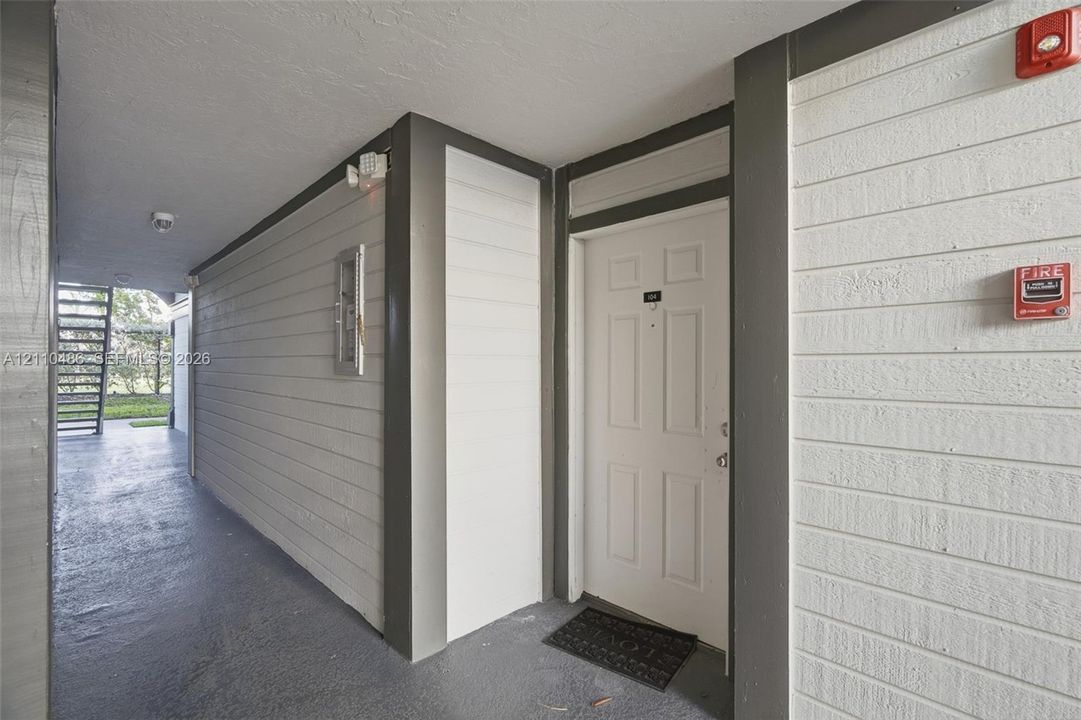 Covered exterior walkway featuring horizontal siding, painted wood trim, and a six-panel entry door
