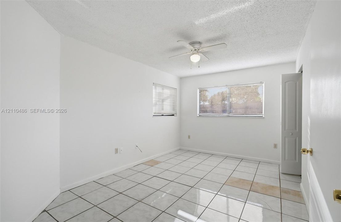 Room featuring white ceramic tile flooring, horizontal slat window blinds, a ceiling fan with light fixture, and a multi-panel interior door