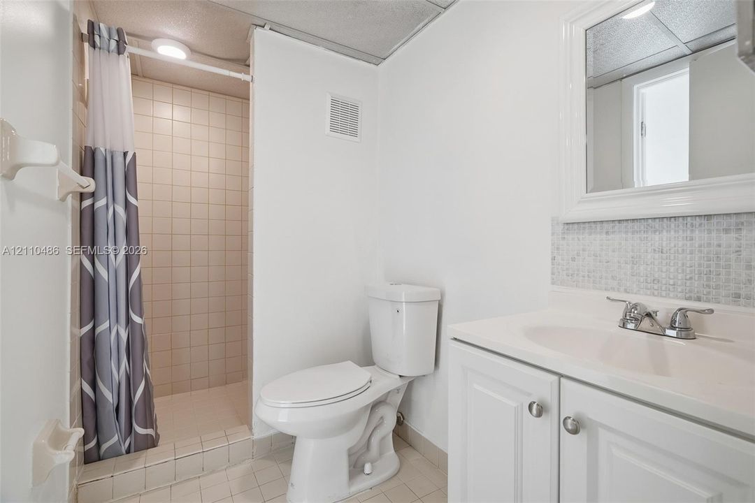Bathroom featuring a white vanity cabinet with an integrated sink, mosaic-tiled backsplash, framed wall mirror, and a walk-in shower with tiled surround