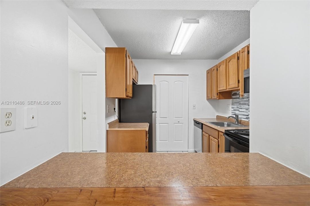 Kitchen featuring natural-finish wood cabinetry, solid-surface countertops, a stainless steel sink, and multi-tone decorative backsplash tile