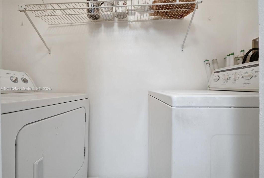 Dedicated laundry area featuring a white top-load washer, front-load dryer, and wall-mounted wire shelving