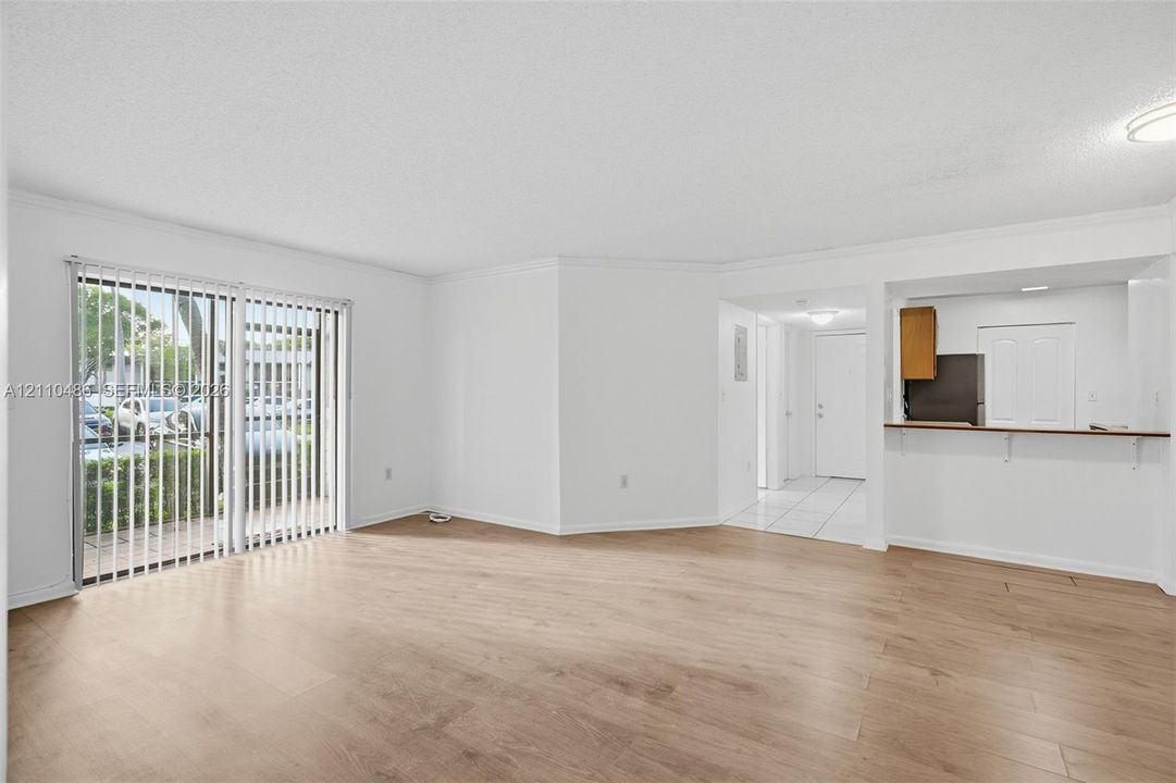 Open-concept interior featuring wood-finish flooring, sliding glass doors with vertical blinds, and a breakfast bar pass-through