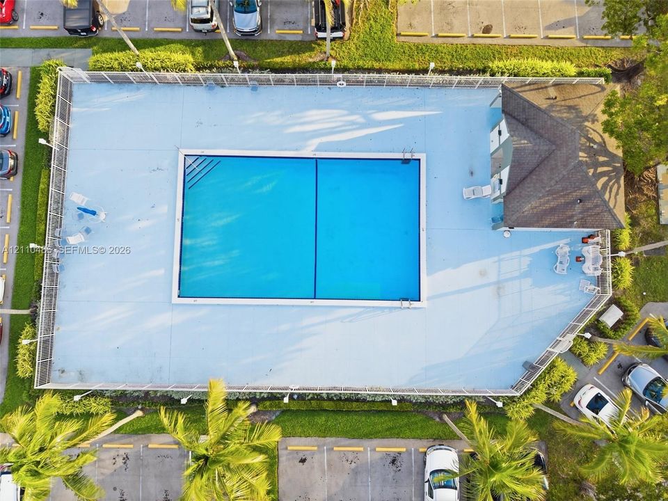Rectangular swimming pool featuring a perimeter fence, surrounding paved deck, and a structure with a shingle roof