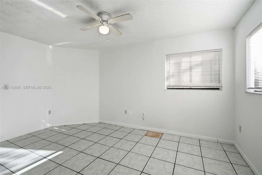 Neutral-toned tile flooring, white wall finishes, ceiling-mounted fan with light fixture, and windows equipped with horizontal blinds